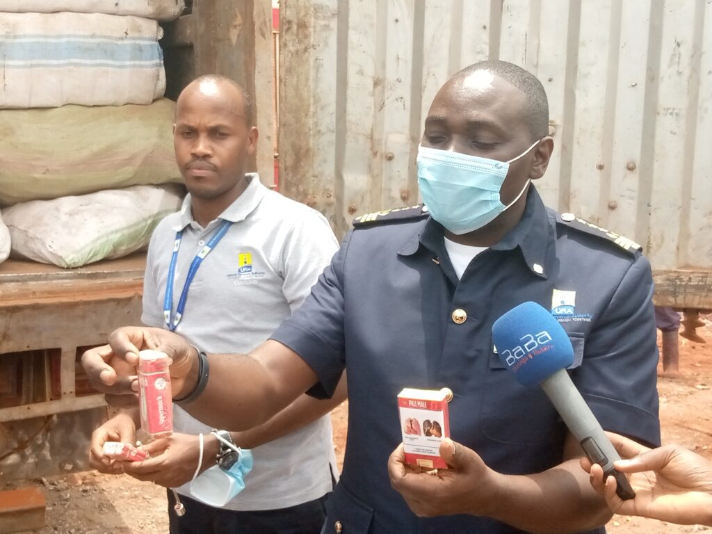 Abel Kagumire Commissioner Customs displays on his right hand an illicit cigarette pack and on his left a legit pack to Journalists