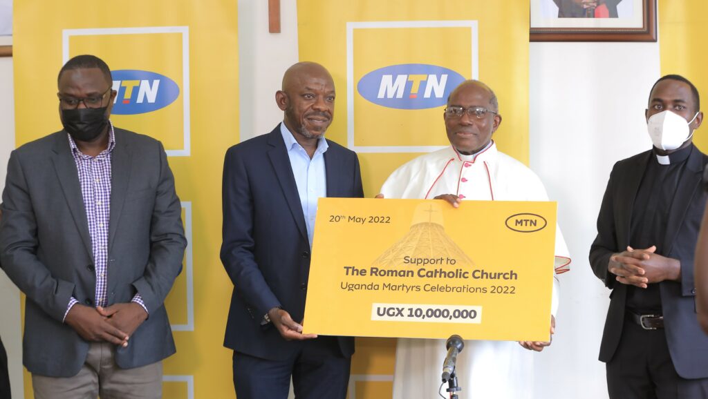 MTN's Michael Ssekadde hands over the Archbishop's cheque to Msgr.Charles Kasibante. The FortP Portal Diocese Cheque shall be handed over next week