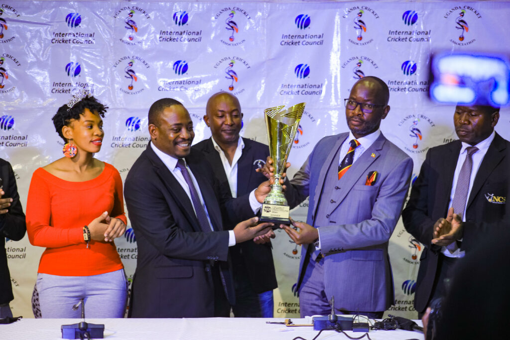 Uganda Cricket Chairman Michael Nuwagaba (2L) presents the trophy that will be competed for to the Minister of State for Sports, Hamson Obua.