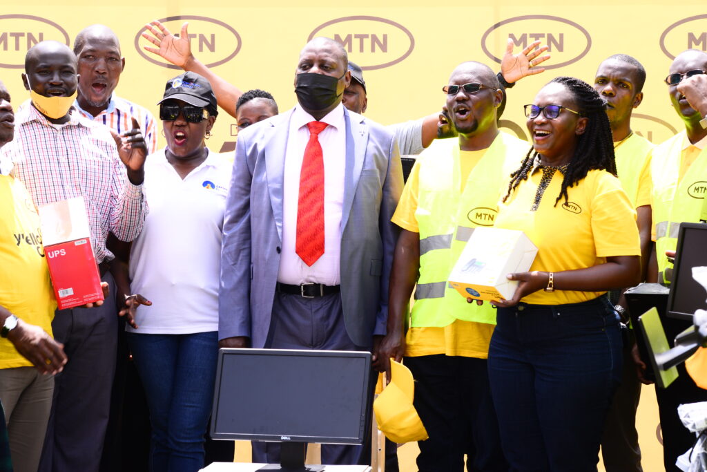 MTN's Dorcas Muhwezi (R) and Kenneth Kiddu (2R) handed over the computers and a WiFi router to UICT's Fred Kitogo (In suit)