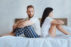 serious-couple-conflict-sitting-bed-trouble-makers-young-people-wearing-pajamas-hands-over-their-knees-looking-94680116
