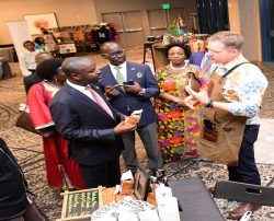 Deputy Speaker Tayebwa (in red tie) listens to the proprietor of Endiro Coffee as he toured stalls at the UNAA convention
