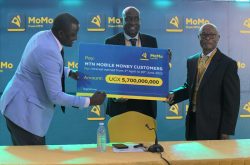 Richard Yego (L) signs the dummy cheque of the total sum of money to be paid out as interest to the active MoMo customers