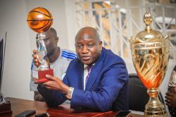 Dr Lawrance Mulindwa with smile while holding East Africa Basketball Girls Trophy