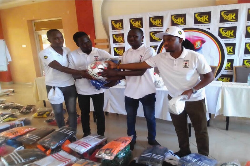 Mutooro (R) is joined by a member of team chairman MK project (L) in handing over a ball and other sports kits to Adjumani team. PHOTO BY ANDREW COHEN AMVESI