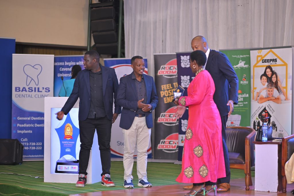 Samuel Bulenzi Isiko, the Stanbic Bank Head of Client Coverage recieving the award from Hon. Amelia Kyambadde, looking on is Robert Mukiza the Director General of Uganda Investment Authority.