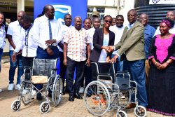 Peace Nyangoma, the Manager of Customer Experience at Stanbic Bank Uganda (in black jacket), handing over a wheelchair to Dr Oscar Kaliisa, the Acting Hospital Director of Fort Portal Referral